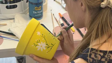 Person painting yellow pot with flowers, indoors.