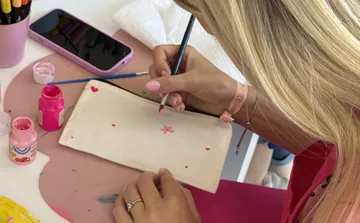 Person painting pink flowers on beige pouch.