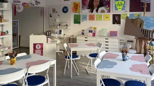 Kunststudio mit Tischen, Stühlen und Gemälden.