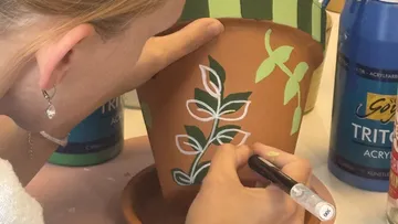 Person painting leaves on terracotta pot.