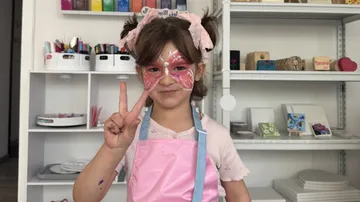 Child with face paint making peace sign indoors.