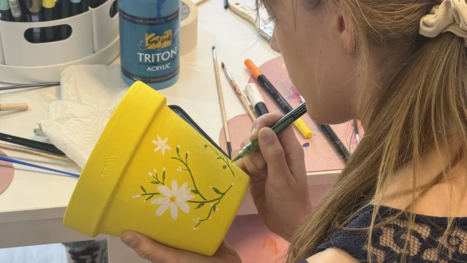 Person painting flower pot at desk.