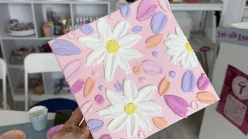 Hand holding daisy painting in studio.