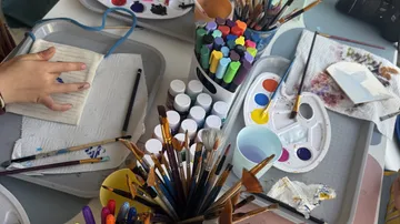 Art supplies and hands creating a painting.