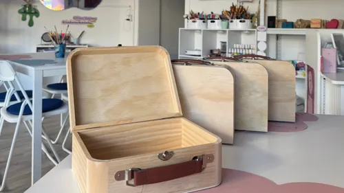 Offene Holzbox auf Tisch, Bastelmaterial im Hintergrund.