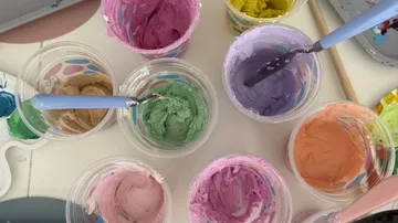 Assorted colorful paints with brushes in cups.