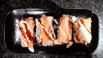 Sushi rolls with sauce on black plate.