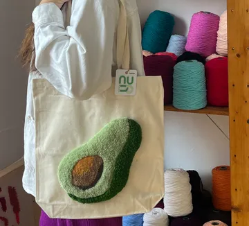 Person holding avocado-design tote, yarn shelves.
