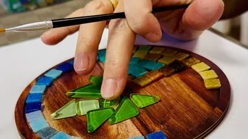 Hand arrangiert Mosaikfliesen auf Holzoberfläche.