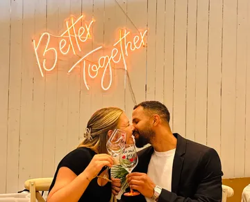 Couple kissing, holding glasses, neon sign.