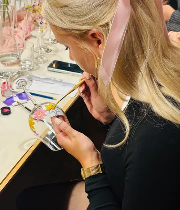 Woman painting wine glass with flowers.