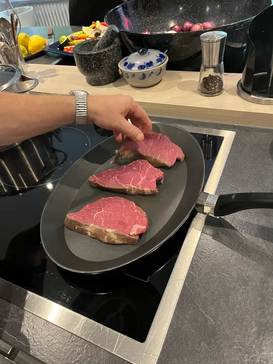 Hand placing steak slices into frying pan.