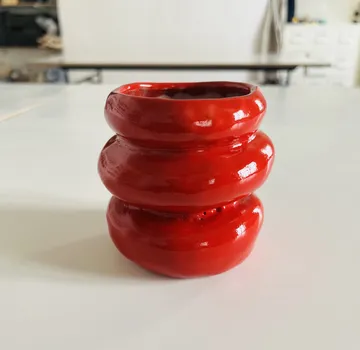 Red ceramic vase on white table.