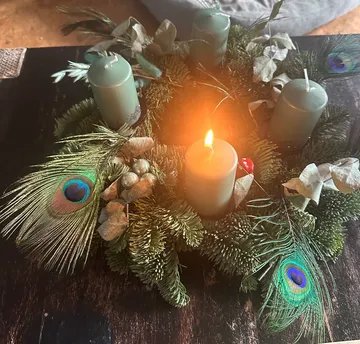 Advent wreath with one lit candle on table.