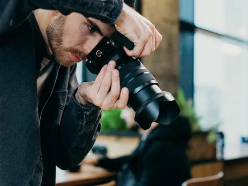 Photographer holds camera, focuses on subject in cafe.