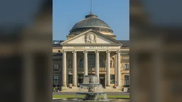 Historisches Gebäude mit Brunnen davor.