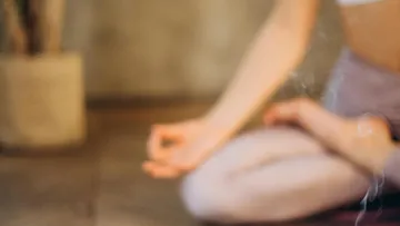 Person meditiert sitzend drinnen, Pflanze in der Nähe.