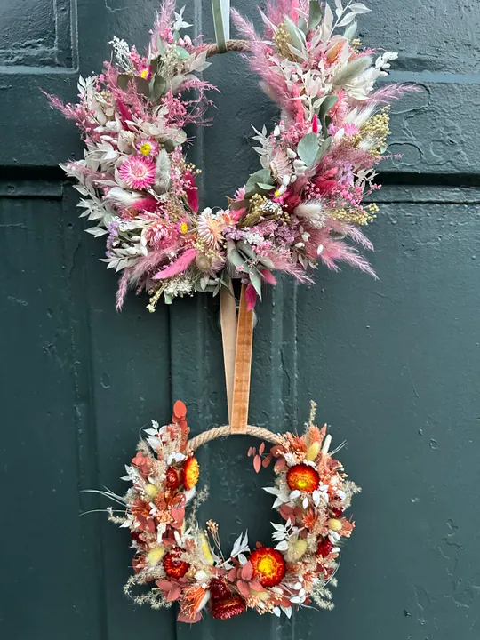 Two floral wreaths hanging on dark wall.