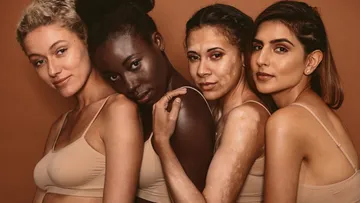 Four women posing together against brown background.