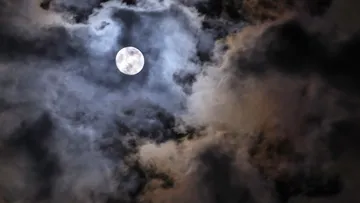 Full moon illuminating cloudy night sky.