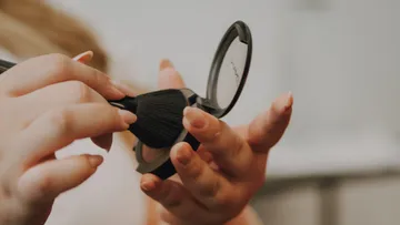 Hands applying makeup with brush.