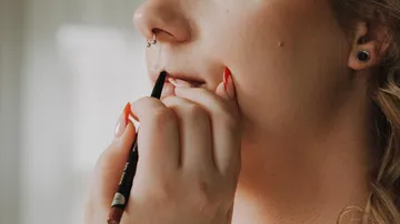 Person applying lip liner, indoor setting.
