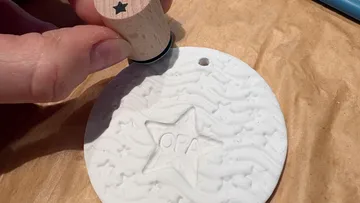 Hand stamps star on white clay ornament.