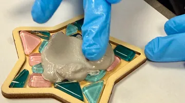 Behandschuhte Hände tragen Mörtel auf Sternmosaik auf.