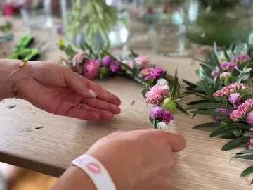 Hands braid colorful flowers on a table.