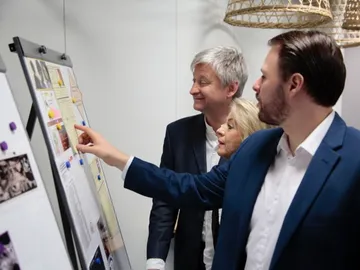 Three people are looking at a bulletin board in an office.