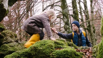 Kind hilft anderem, moosige Felsen im Wald zu erklimmen.