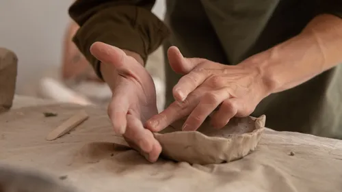 Hands sculpting clay on a table surface.