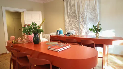 Rote Tische mit Büchern und Blumen im Raum.