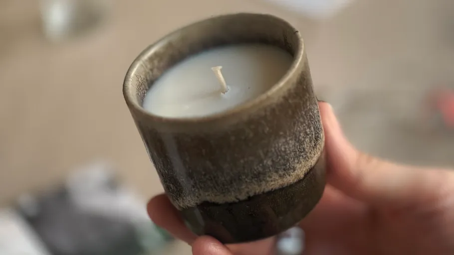 Hand hält eine kleine, unbeleuchtete Kerze drinnen.
