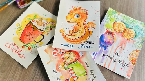 Hand-painted holiday cards on wooden table.