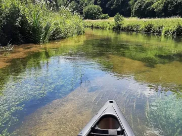 Canoe floats on clear water in quiet surroundings.