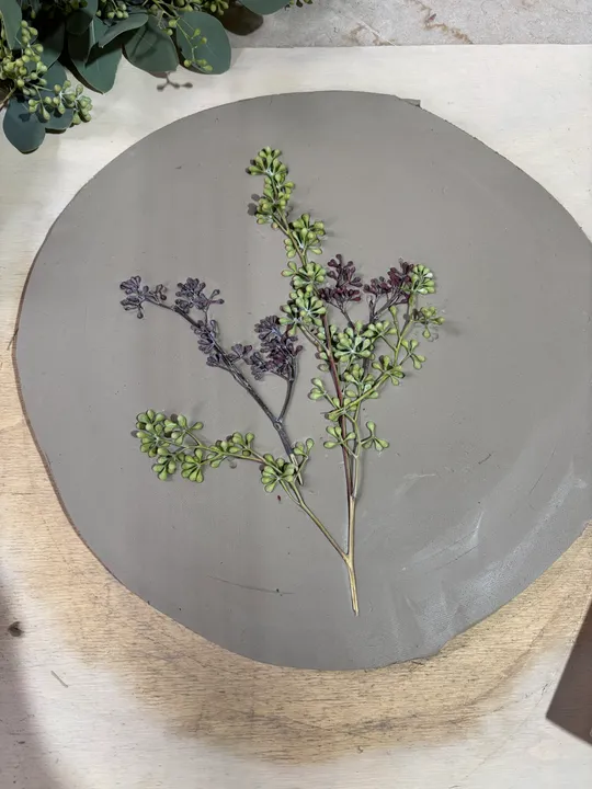 Gepresste Blume auf runder Tonscheibe.