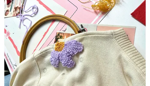 Stickblume auf beigem Pullover, Basteltisch.