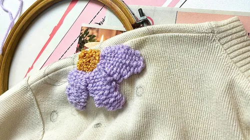 Stickblume auf beigem Pullover, Basteltisch.