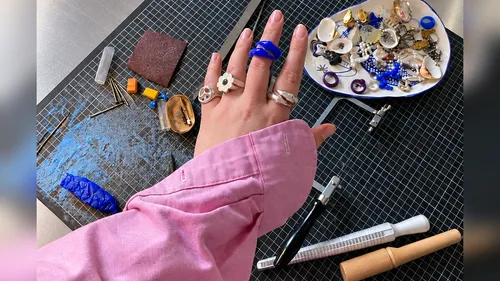 Hand mit Ringen fertigt Schmuck auf Tisch.