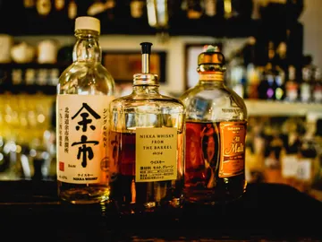 Drei Whiskyflaschen stehen auf einem Tisch in einer Bar.