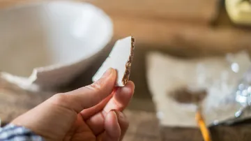 Hand holding pottery piece indoors.
