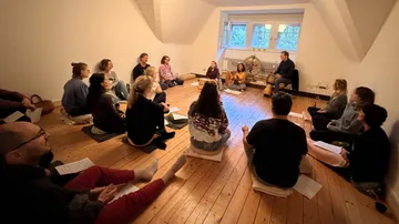 People sitting in circle, discussing in a room.