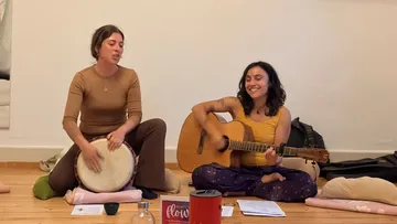 Two women play guitar and drum indoors.