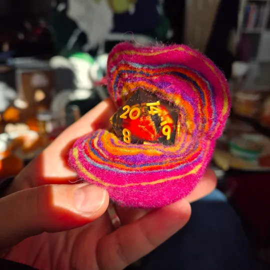 Hand hält bunten Stoff mit Würfel darin.