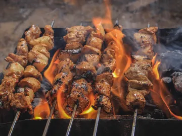 Meat skewers sizzle over a blazing fire on a grill.