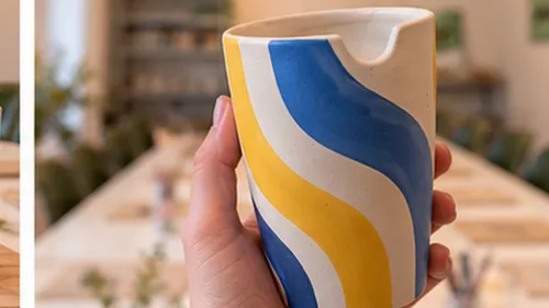 Hand hält bunten Keramikbecher drinnen.