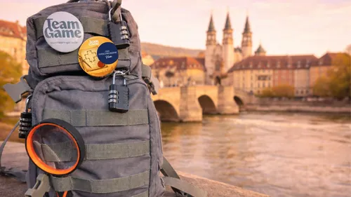 Rucksack mit Abzeichen vor Fluss und Brücke.