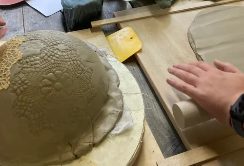 Hands working clay with rolling pin.