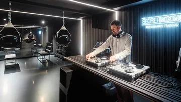 DJ spielt Musik im modernen Fitnessstudio mit Neonschild.